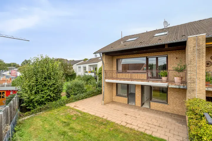 Rückansicht eines Mehrfamilienhauses mit Balkon und Gartenfläche